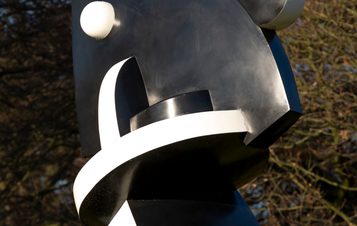Close up of a black and white abstract sculpture displayed on plinths outdoors, with trees behind it.