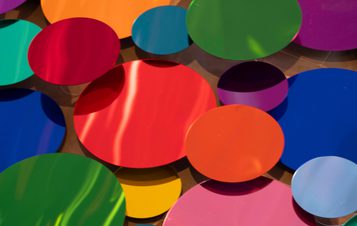 An installation of colourful mirrored discs, displayed at different heights to catch reflections.