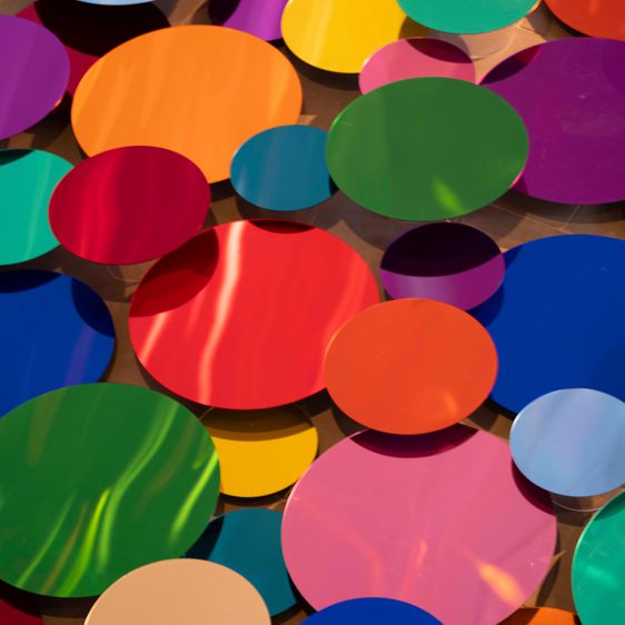 An installation of colourful mirrored discs, displayed at different heights to catch reflections.