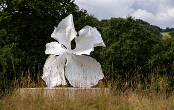 A sculpture of a white orchid flower, displayed on a concrete plinth outdoors.