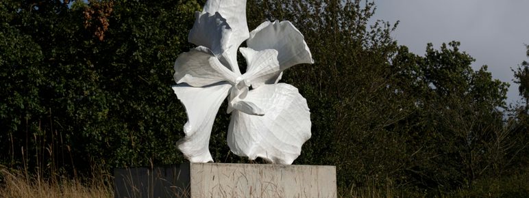A sculpture of a white orchid flower, displayed on a concrete plinth outdoors.