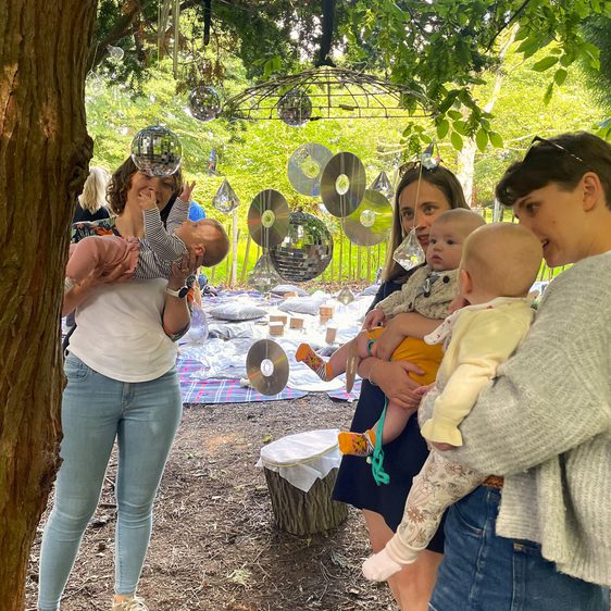 A group of adults and babies playing with suspended shiny discs outdoors