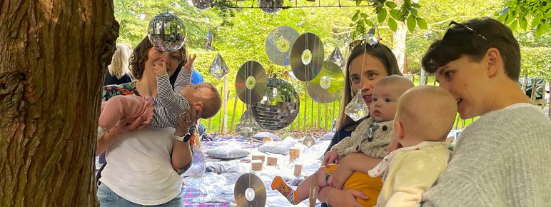 A group of adults and babies playing with suspended shiny discs outdoors