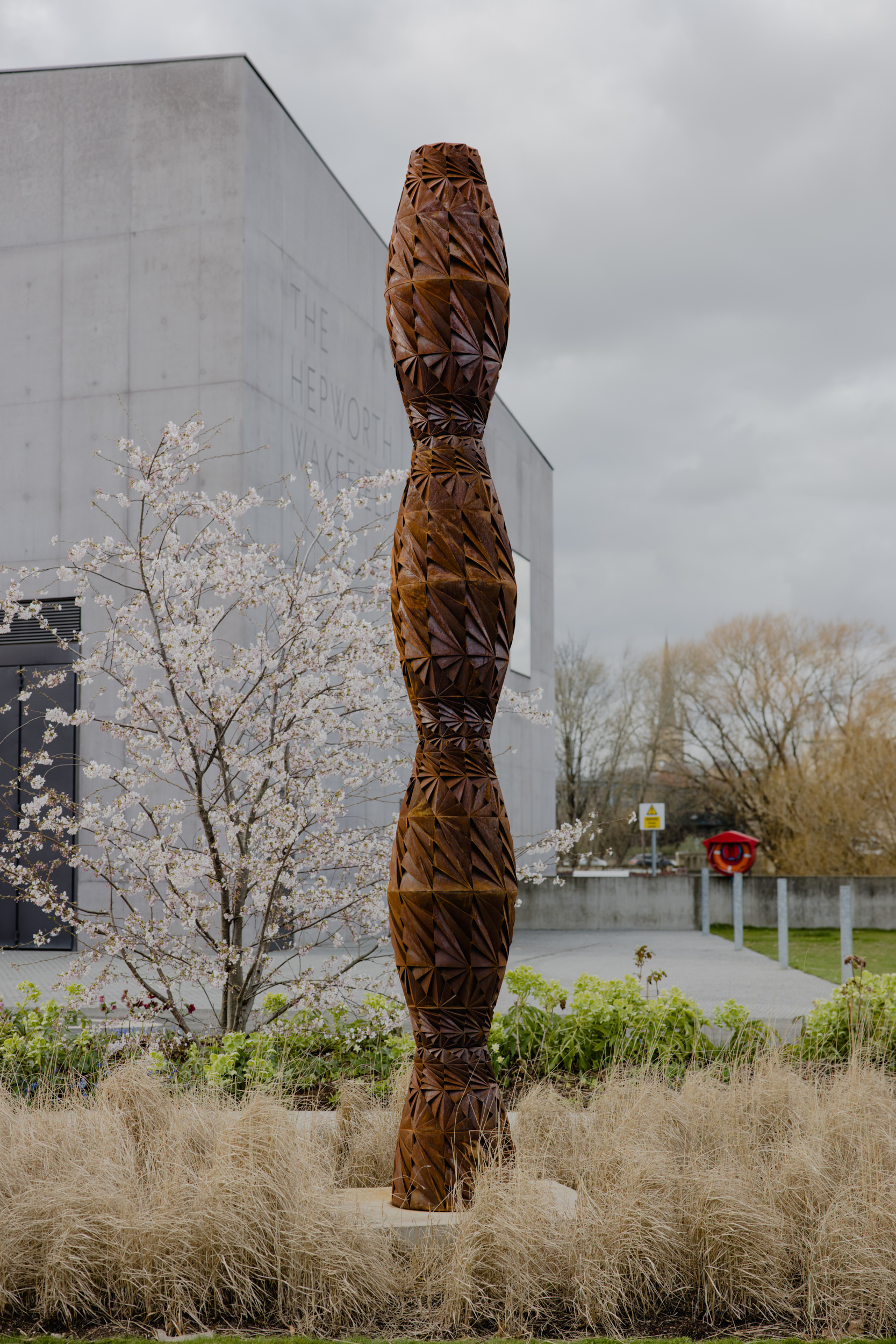 A tall thin bronze sculpture in a garden