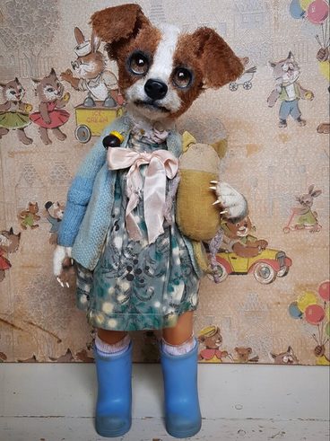 A whimsical handmade doll resembling a dog, dressed in a floral dress and a blue cardigan. It holds a small stuffed animal and wears blue wellington boots. The background features a vintage pattern with playful animal illustrations.