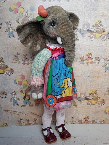 A whimsical stuffed elephant doll stands upright, wearing a colourful dress with an elephant print. The doll has large ears, a small horn on its head, and is accessorised with a bow. The background features playful vintage illustrations of children and animals.