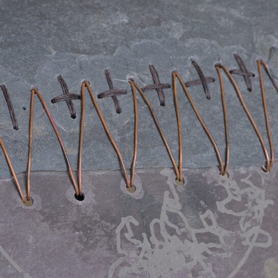 An art installation featuring a large black-and-white mural of a tree, a wooden bench, and various sculptures. The space includes a white pedestal displaying a red fabric piece and photographs arranged on a nearby shelf.