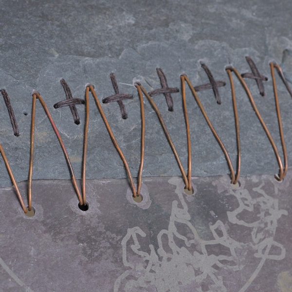 An art installation featuring a large black-and-white mural of a tree, a wooden bench, and various sculptures. The space includes a white pedestal displaying a red fabric piece and photographs arranged on a nearby shelf.