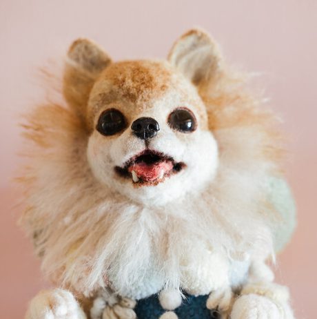Vintage, plush dog puppet with a fluffy, brown and white coat, wearing a blue dress and frilled collar. The puppet has a smiling expression.