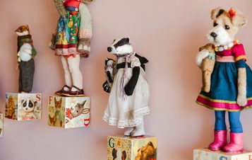 A collection of vintage, hand-stitched badger and dog figures stands on colourful alphabet blocks against a pink wall.