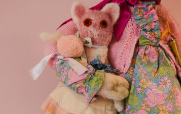 A rag doll holds a small, plush mouse in a colourful floral dress. The doll has white tights and pink shoes.