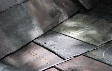 Close-up shot of several weathered slate tiles stacked together. The tiles display a grid pattern and the word “Slate” in gold lettering. A weathered, textured surface.