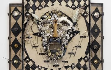 A wall based sculpture of a face surrounded by harlequin patterns